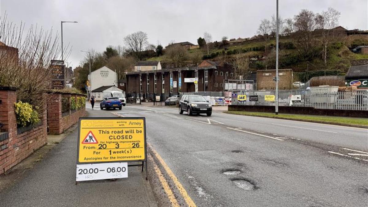 A road with several potholes on it with a temporary yellow sign on the left saying 'this road will be closed' for highways improvements from 20 March for one week between 8pm and 6am.